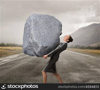 Under pressure of difficulties. Attractive businesswoman carrying with effort big heavy stone