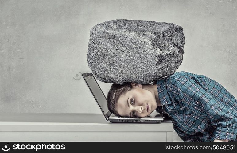 Under pressure of work. Woman programmer pressed with heavy stone to laptop