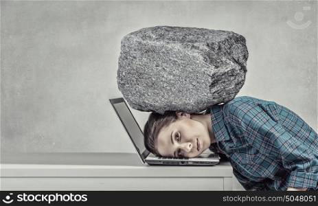 Under pressure of work. Woman programmer pressed with heavy stone to laptop