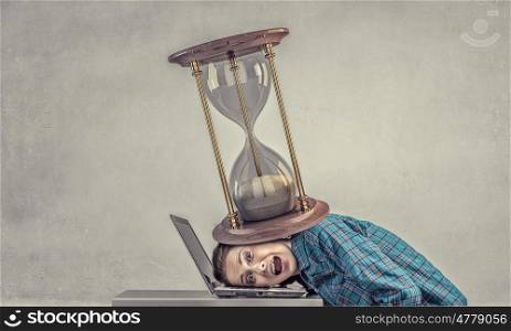Under pressure of work. Woman programmer pressed with sandglass to laptop