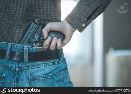 Undercover police agent is holding a black hidden weapon in his hand