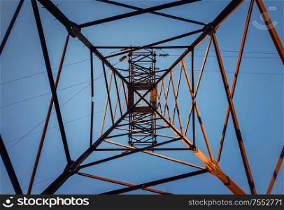 Underneath a truss pillar construction. Different geometric shapes, patterns of a steel structure. Metallic texture of an electricity pole.