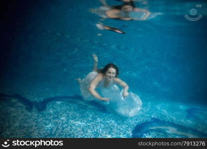 Underwater shot in motion of sexy woman swimming in deep pool in white dress