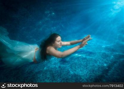 Underwater shot of beautiful woman in dress comes up from pool at beam of light
