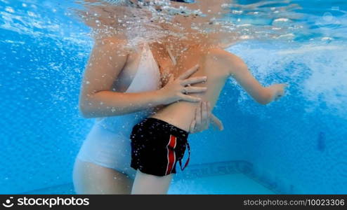 Underwater shot young mother supporting an dholding her little son learning how to swim in swimming pool. Concept of family healthcare and sports. Underwater shot young mother supporting an dholding her little son learning how to swim in swimming pool. Concept of family healthcare and sports.