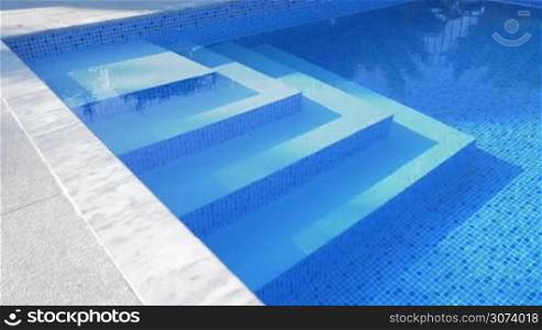 Underwater stairs in outdoor blue tiled swimming pool with clear water. Spa and resort