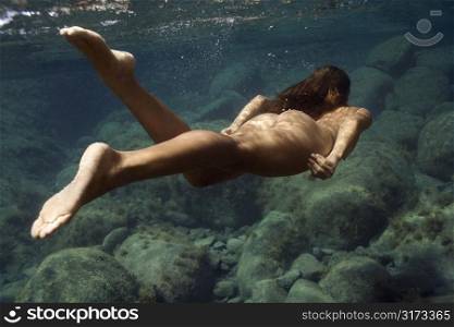 Underwater view of young Asian nude woman swimming away.