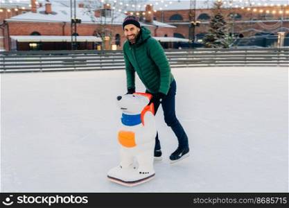 Unexperienced male going to learn skating skills, uses skate aid for being in balance on ice rink and not fall, expresses positive emotions and enjoyment, rejoices winter holidays. Entertainment