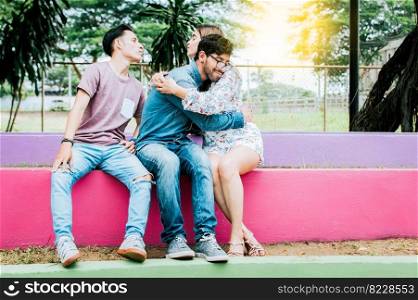 Unfaithful girl sitting hugging her boyfriend and secretly kissing another man. Unfaithful girlfriend hugging her boyfriend in a park secretly kissing another man, Couple infidelity concept