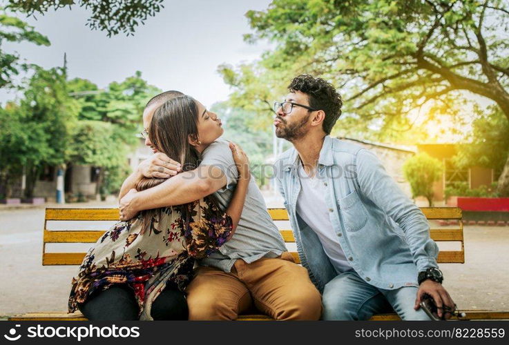 Unfaithful woman sitting hugging her boyfriend and secretly kissing another man. Unfaithful girlfriend hugging her boyfriend in a park secretly kissing another man, Couple infidelity concept