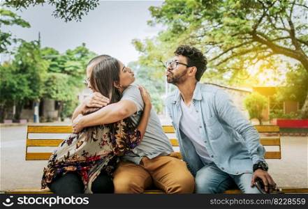 Unfaithful woman sitting hugging her boyfriend and secretly kissing another man. Unfaithful girlfriend hugging her boyfriend in a park secretly kissing another man, Couple infidelity concept