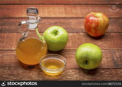 unfiltered, raw apple cider vinegar with mother - a cruet with a small glass bowl surrounded by fresh apples on rustic wood