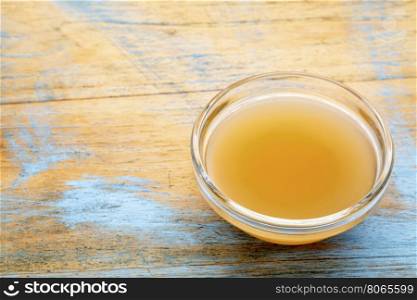 unfiltered, raw apple cider vinegar with mother - a small galls bowl against wood with a copy space