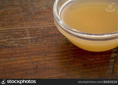 unfiltered, raw apple cider vinegar with mother - a small glass bowl against rustic wood with a copy space