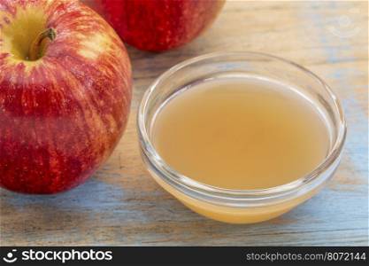 unfiltered, raw apple cider vinegar with mother - a small glass bowl with fresh red apples