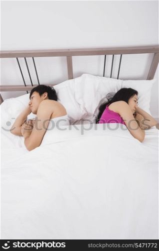 Unhappy Asian couple sleeping back to back in bed