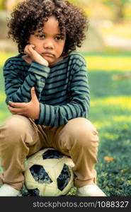 Unhappy bored little african american kid sitting in the park. The boy showing negative emotion. Child trouble concept.