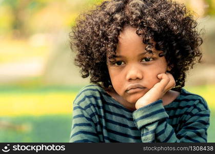 Unhappy bored little african american kid sitting in the park. The boy showing negative emotion. Child trouble concept.. Unhappy little african american kid in the park.