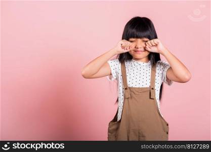 Unhappy children. Asian little kid 10 years old bad mood her cry wipe tears with fingers at studio shot isolated on pink background, child girl stress feeling sad unhappy crying