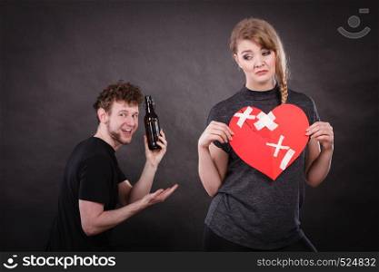 Unhappy couple. Family and alcoholism problems. Addiction and trouble of drinking. Man with alcohol bottle. Sad woman holds paper broken heart.. Sad woman and man addicted to alcohol. Broken heart.