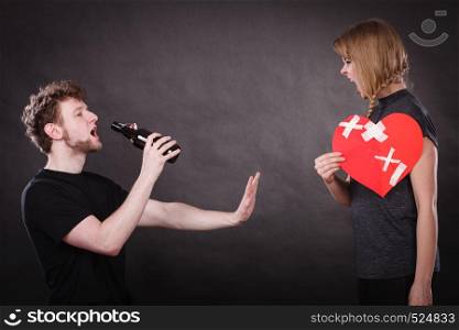 Unhappy couple. Family and alcoholism problems. Addiction and trouble of drinking. Man with alcohol bottle. Angry woman screaming holds paper broken heart.. Angry woman and man addicted to alcohol. Broken heart.