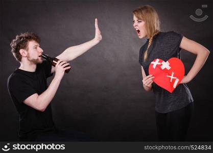 Unhappy couple. Family and alcoholism problems. Addiction and trouble of drinking. Man with alcohol bottle. Angry woman screaming holds paper broken heart.. Angry woman and man addicted to alcohol. Broken heart.
