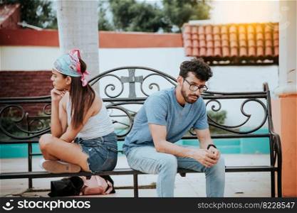 Unhappy couple sitting back to back on bench. Concept of couple problems and crisis. Upset young couple sitting back to back in a park, Young couple arguing sitting back to back on a bench