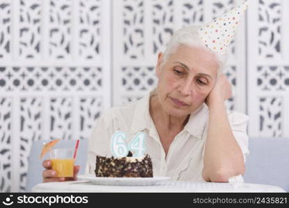 unhappy elder woman looking her birthday cake holding glass juice hand