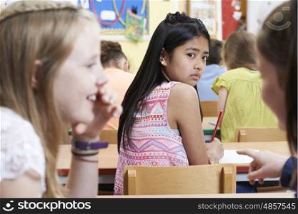 Unhappy Girl Being Gossiped About By School Friends In Classroom