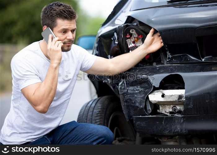 Unhappy Male Driver With Damaged Car After Accident Calling Insurance Company On Mobile Phone
