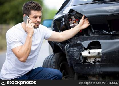 Unhappy Male Driver With Damaged Car After Accident Calling Insurance Company On Mobile Phone