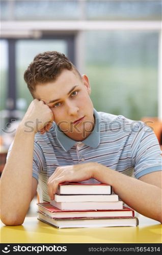 Unhappy Male Student Studying In Classroom With Books