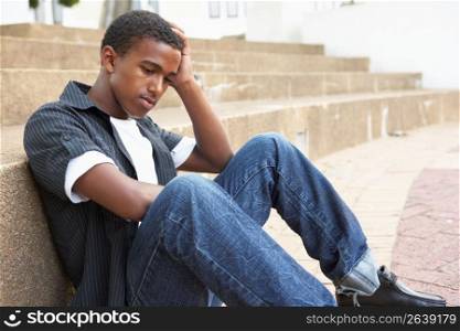 Unhappy Male Teenage Student Sitting Outside On College Steps