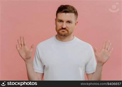 Unhappy man in white t-shirt rejects proposition, shows refusal gesture, isolated on pink background