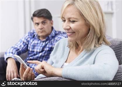 Unhappy Man Sitting On Sofa As Partner Uses Mobile Phone