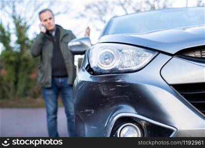 Unhappy Mature Male Driver With Damaged Car After Accident Calling Insurance Company On Mobile Phone