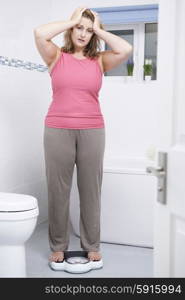 Unhappy Overweight Woman Weighing Herself On Scales In Bathroom