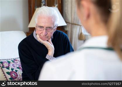 Unhappy Senior Man Being Visited By Female Nurse