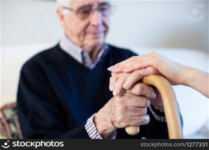 Unhappy Senior Man With Hands On Walking Stick Being Comforted By Woman Health Visitor