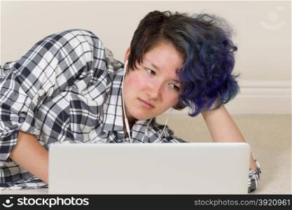 Unhappy teen girl looking at computer while listening to music at home.