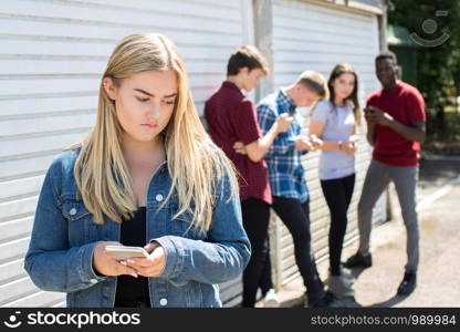 Unhappy Teenage Girl Being Bullied By Text Message Outdoors