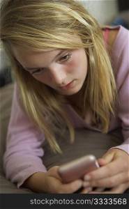 Unhappy Teenage Girl Lying In Bedroom With Mobile Phone
