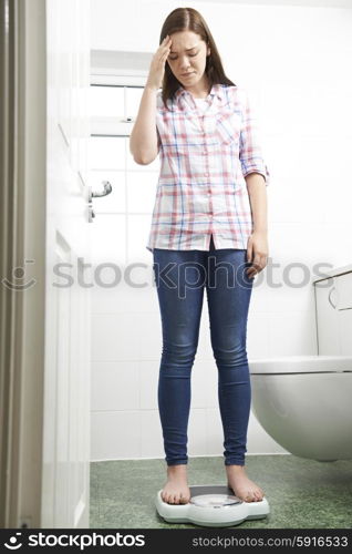 Unhappy Teenage Girl Standing On Bathroom Scales