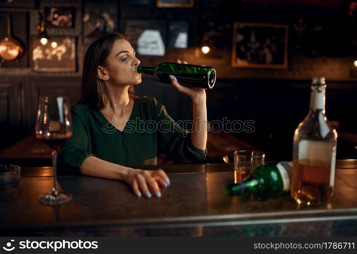 Unhappy woman drinks alcohol beverage at the counter in bar. One female person in pub, human emotions, leisure activities, depression. Unhappy woman drinks alcohol at the counter in bar