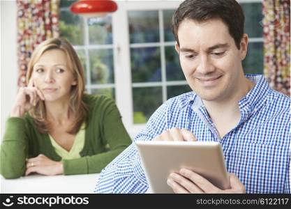 Unhappy Woman Sitting At Table As Partner Uses Digital Tablet