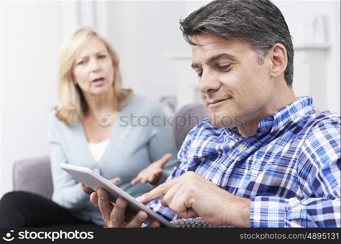 Unhappy Woman Sitting On Sofa As Partner Uses Digital Tablet