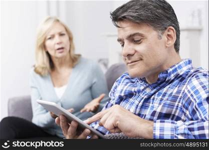 Unhappy Woman Sitting On Sofa As Partner Uses Digital Tablet