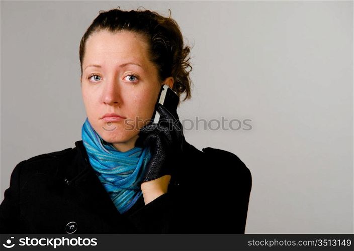 unhappy woman with mobile phone in black coat on gray background