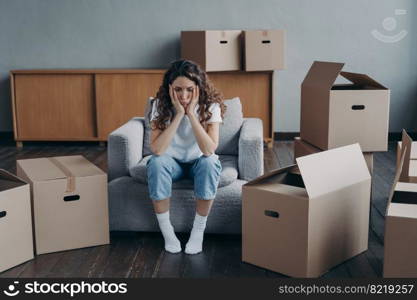 Unhappy young woman sitting in empty room near cardboard boxes feel unmotivated to pack her belongings. Spanish girl is sad because of relocation. Hard moving day, divorce concept.. Unhappy woman is sad because of relocation sitting near cardboard boxes. Hard moving day, divorce