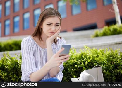 Unhappy Young Woman With Mobile Phone Being Bullied Online On Universtiy Campus